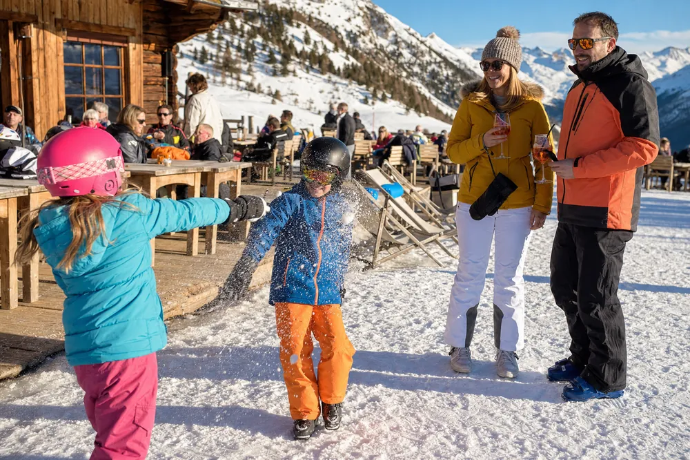 Enfants en casque de ski jouant dans la neige devant un restaurant d'altitude