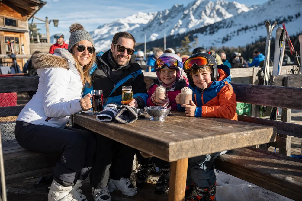 Famille avec un chocolat chaud sur une terrasse ensoleillée au bord des pistes