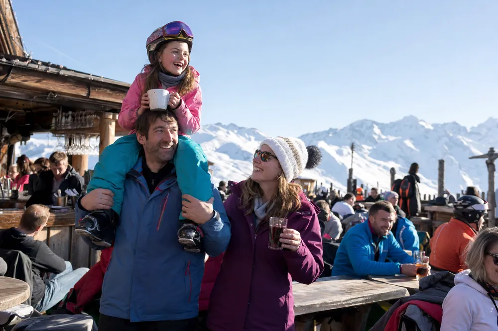 Un père porte sa fille sur ses épaules sur une terrasse ensoleillée dans les Alpes